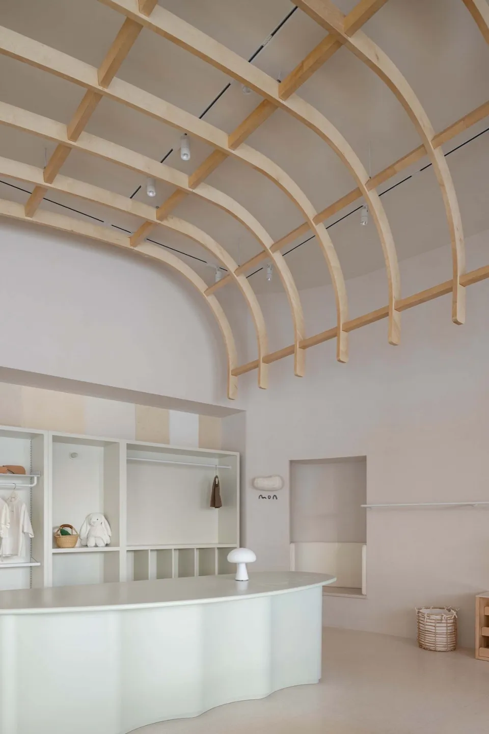 A minimalist clothing shop with a curved wooden counter and exposed wooden beams on the ceiling.