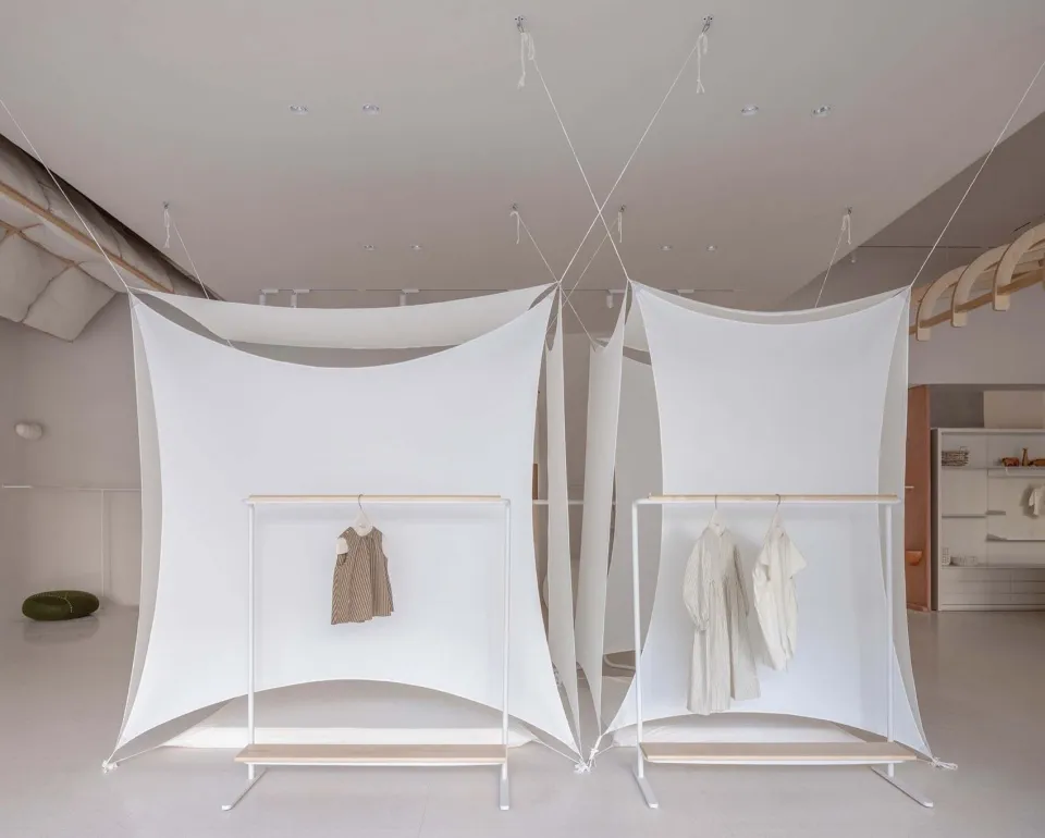 A minimalist retail display featuring white clothing racks with white clothing hung on them, all enclosed by white fabric pan
