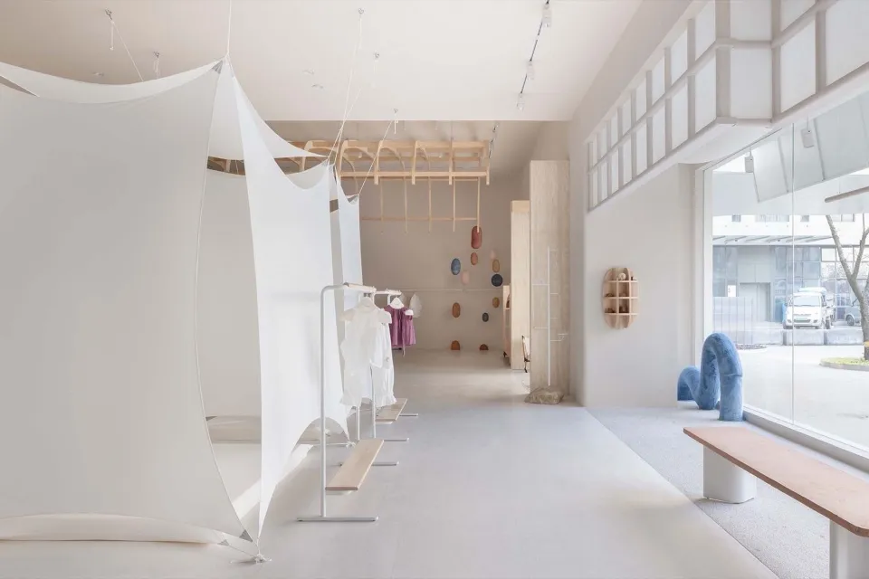 Interior design of a minimalist clothing shop featuring white architectural elements and neutral-colored materials.