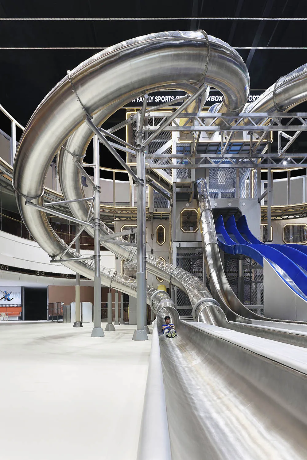 Person sliding down a metallic, spiraling water slide in an amusement park