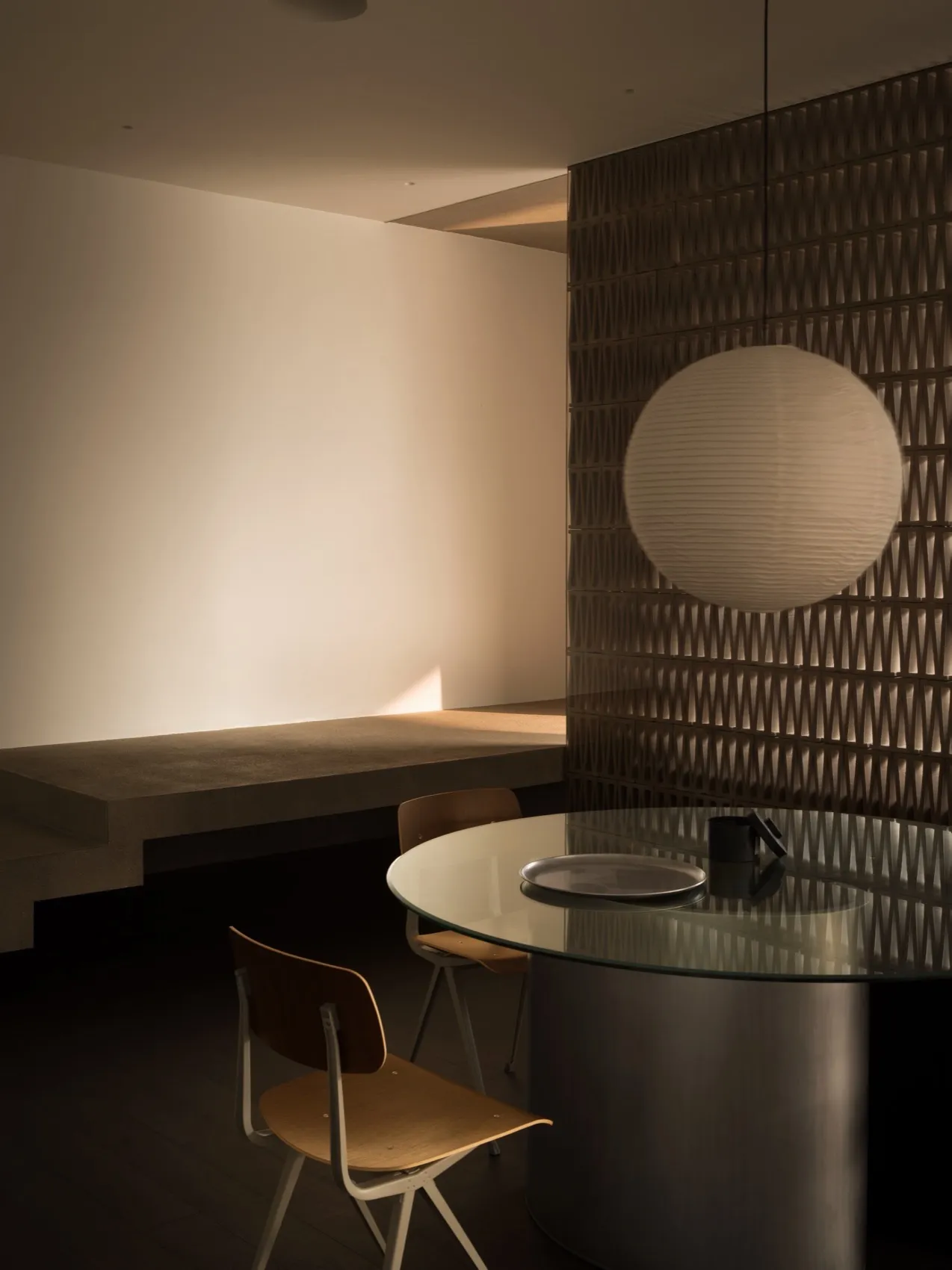 Modern minimalist dining room with glass table and pendant light fixture.