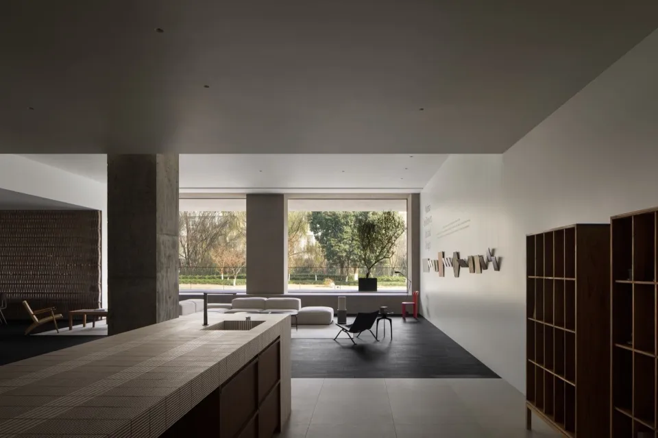 A modern living room with concrete walls and floors, featuring minimalistic furniture and large windows.