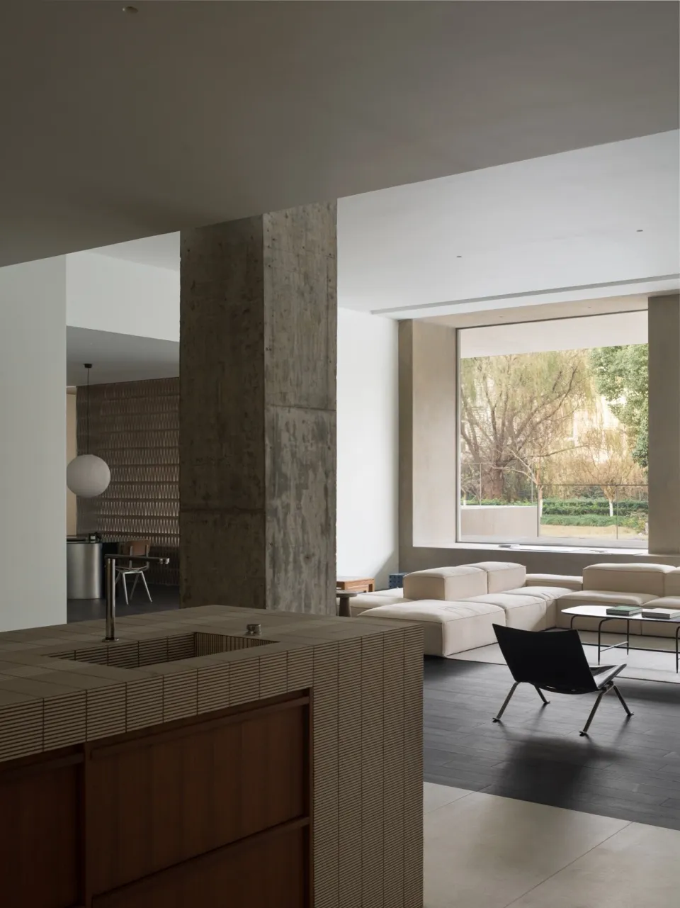 Modern minimalist living room with exposed concrete columns and large windows.