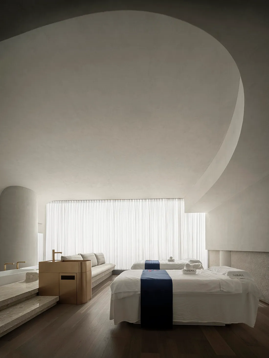 A minimalist bedroom with white, subtly textured walls and a dark wooden floor.