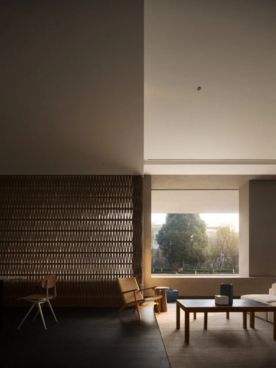 Minimalist living room with wooden floor, furniture, and large window showing outdoor scenery.