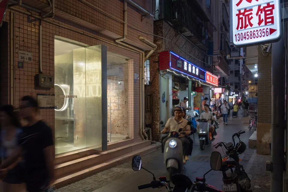 繁忙的街景,建築由磚、玻璃與金屬構成,搭配機車與霓虹燈招牌。