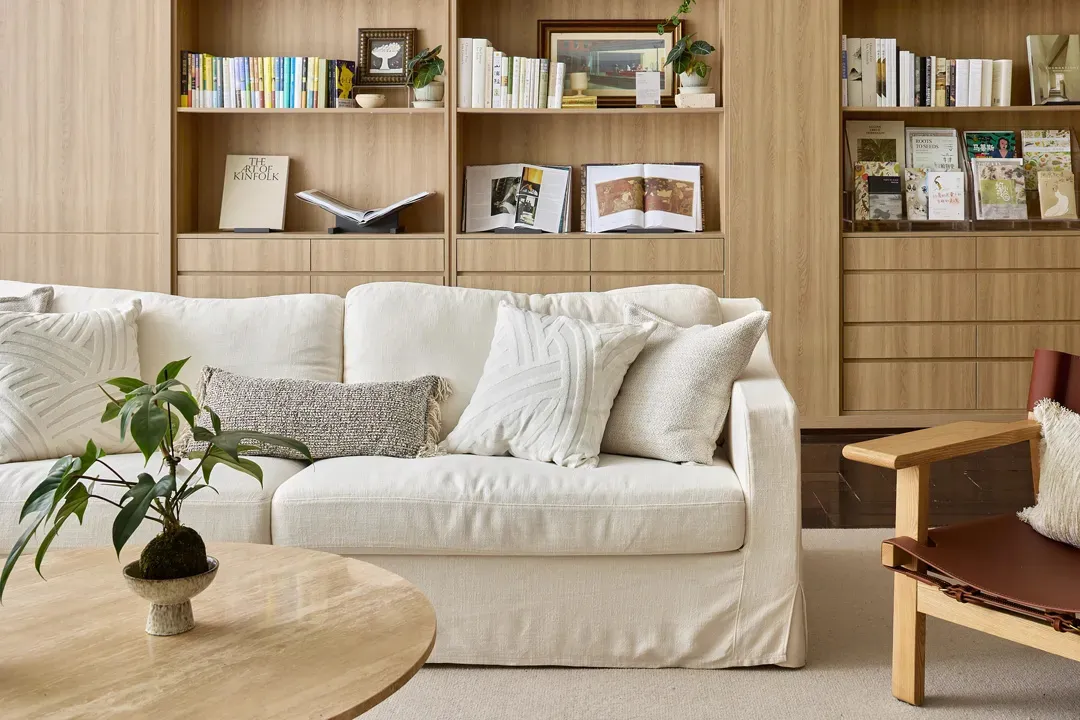 A comfortable white living room with a cozy sofa, bookshelves, and a round wooden coffee table.
