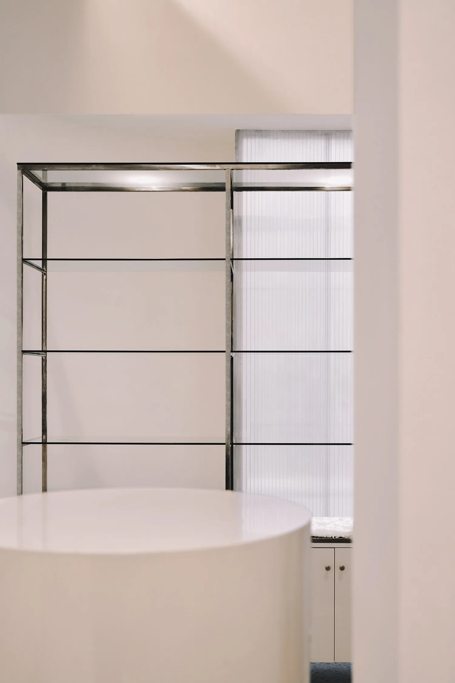 A minimalist interior design featuring glass shelves against a white wall.