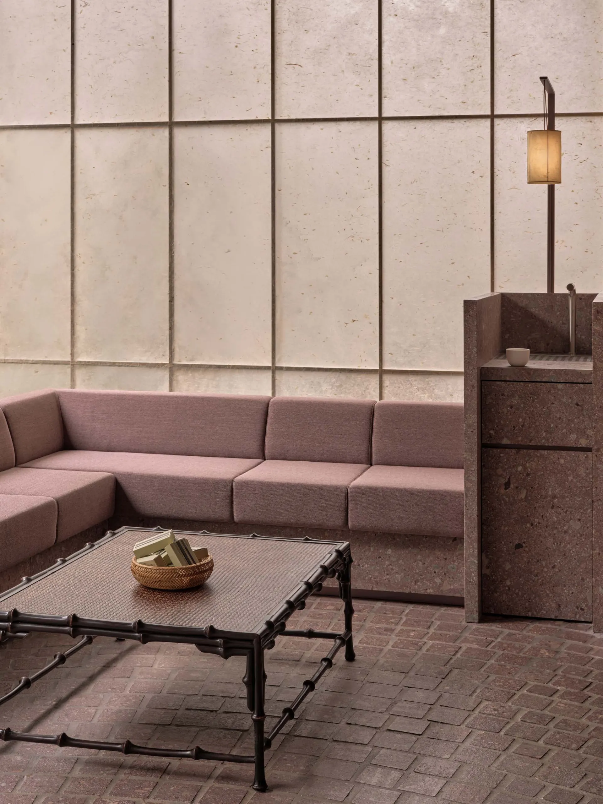 A modern living room with a pink upholstered sofa, a textured table, and a lamp with a paper lampshade.
