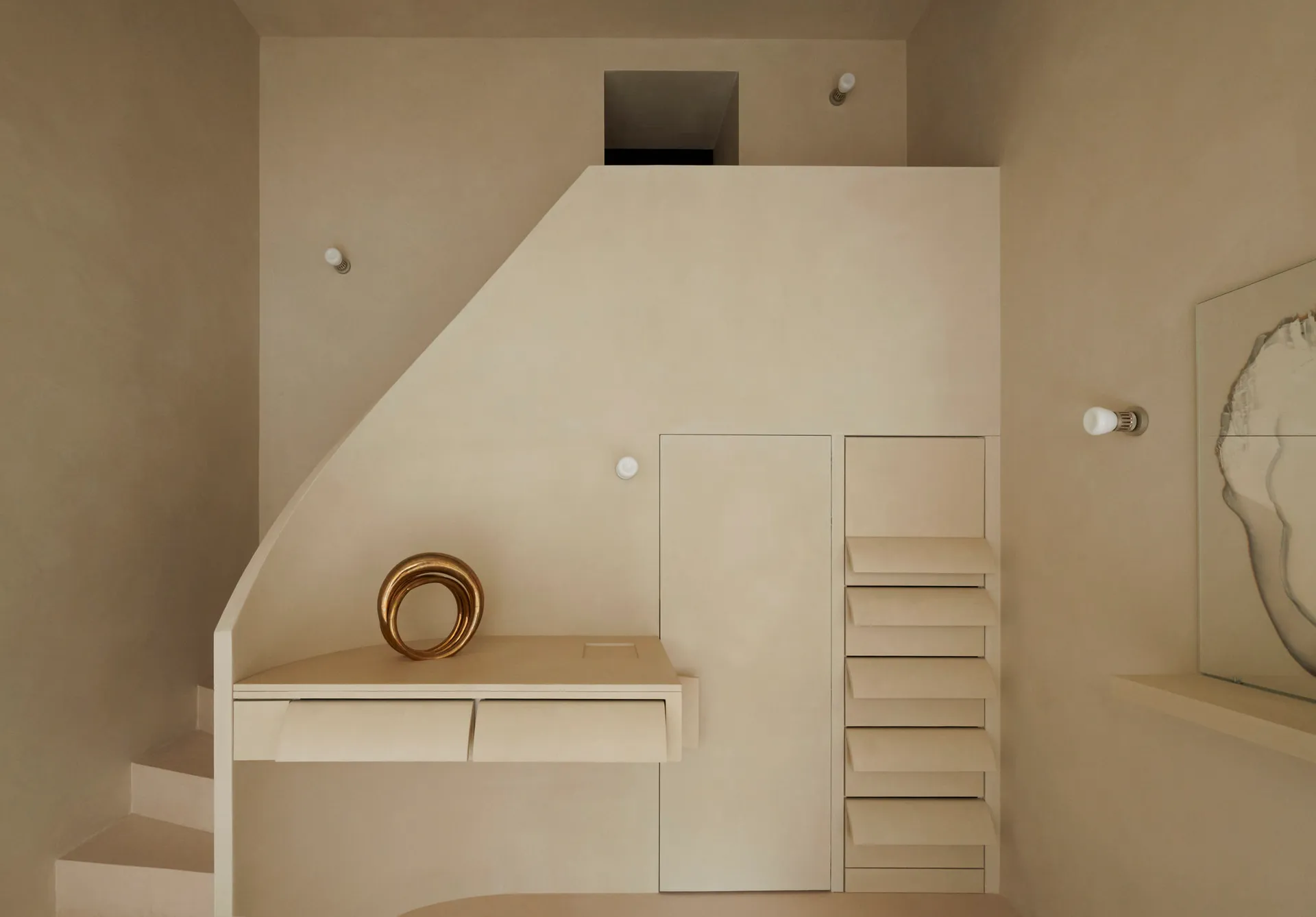 A minimalist white interior space with steps, a desk, and a metallic sculpture.
