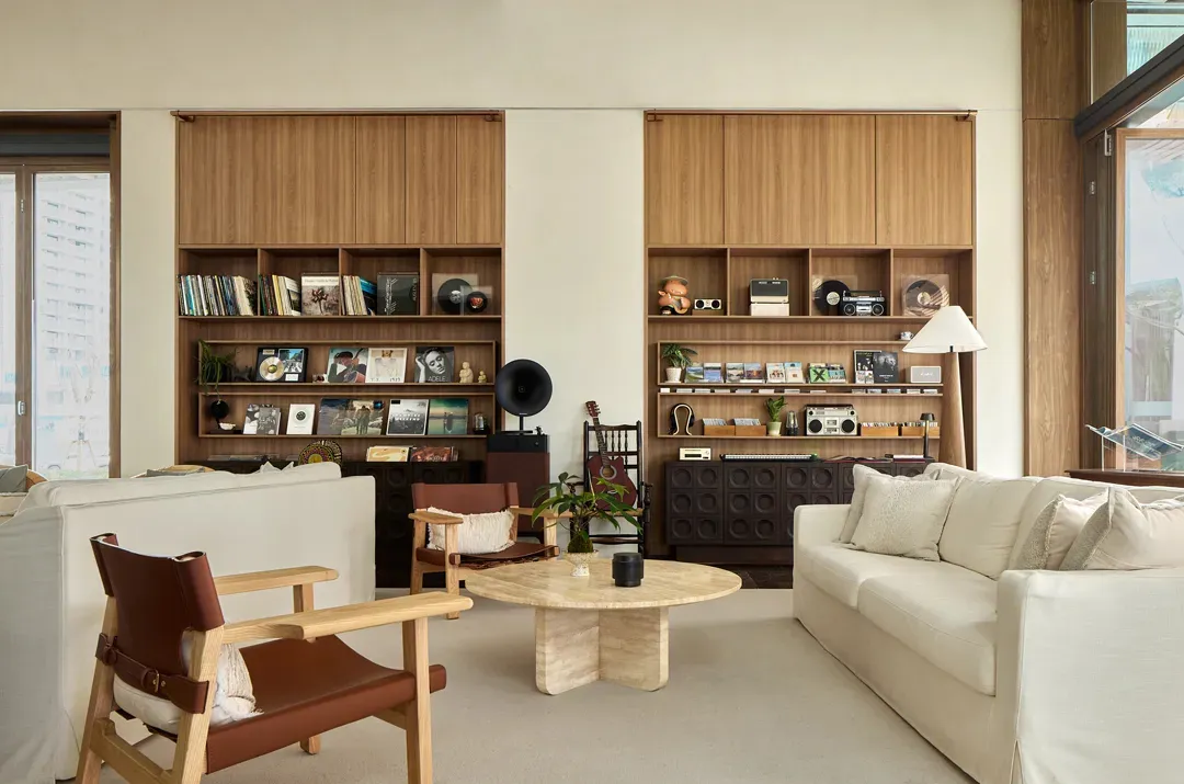 A modern living room with a comfortable sofa, chairs, and wooden shelves displaying books, records, and other decorative item