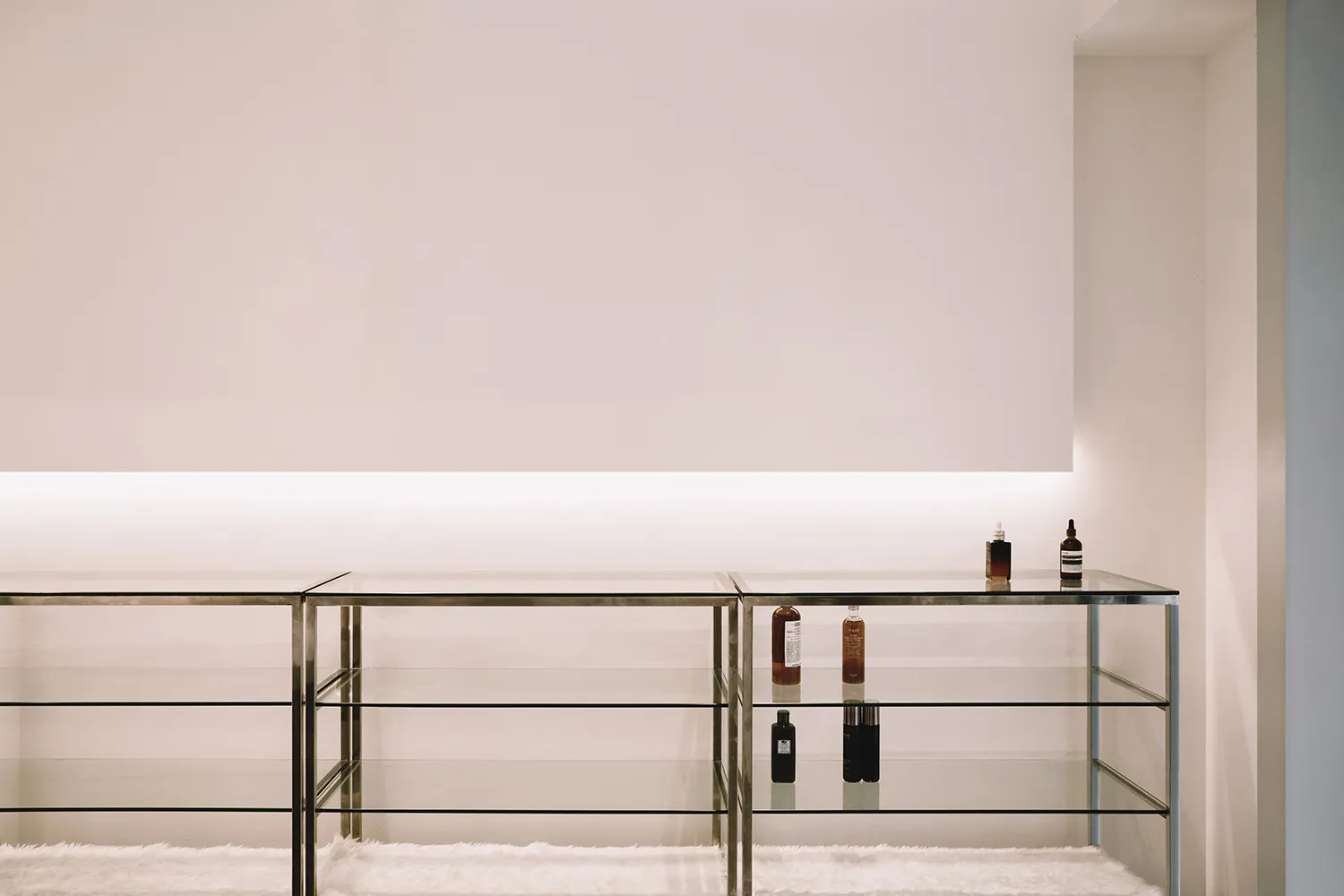 A minimalist retail storefront with glass walls and shelves displaying products.