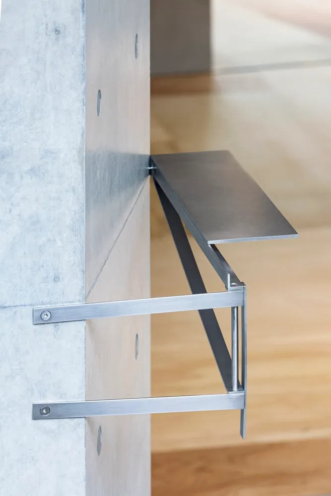 A metal bracket mounted on a concrete wall with a horizontal metal shelf.