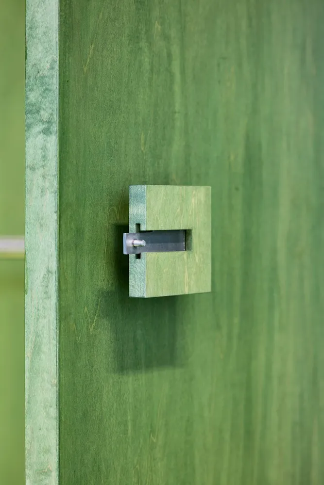 Close-up of a minimalist green door handle mounted on a green wooden door.