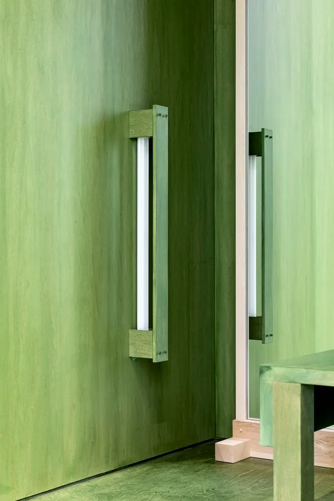 Modern interior design featuring a wooden door handle against a green wooden wall.