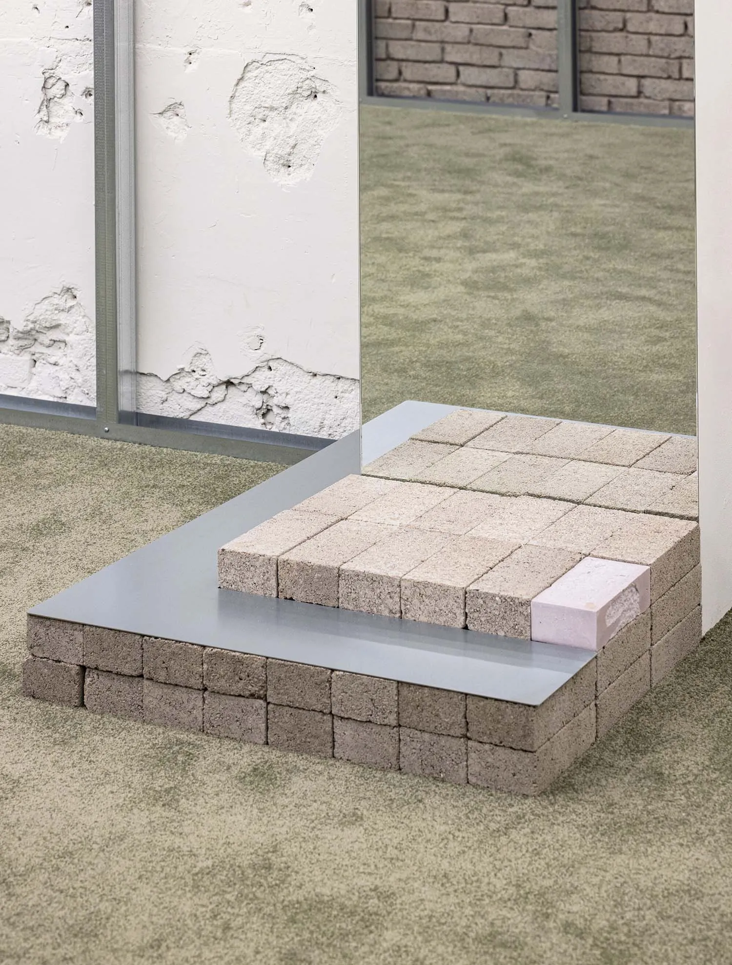 A minimalist installation featuring bricks arranged in a grid pattern on a step-like structure.