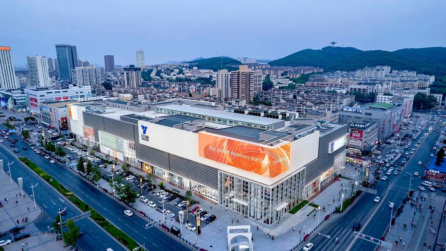 Aerial view of a modern cityscape featuring buildings with glass facades and mixed materials, with mountains in the backgroun