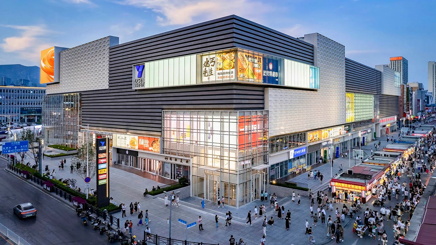 Modern shopping mall exterior with glass walls, concrete foundations, and aluminum beams.