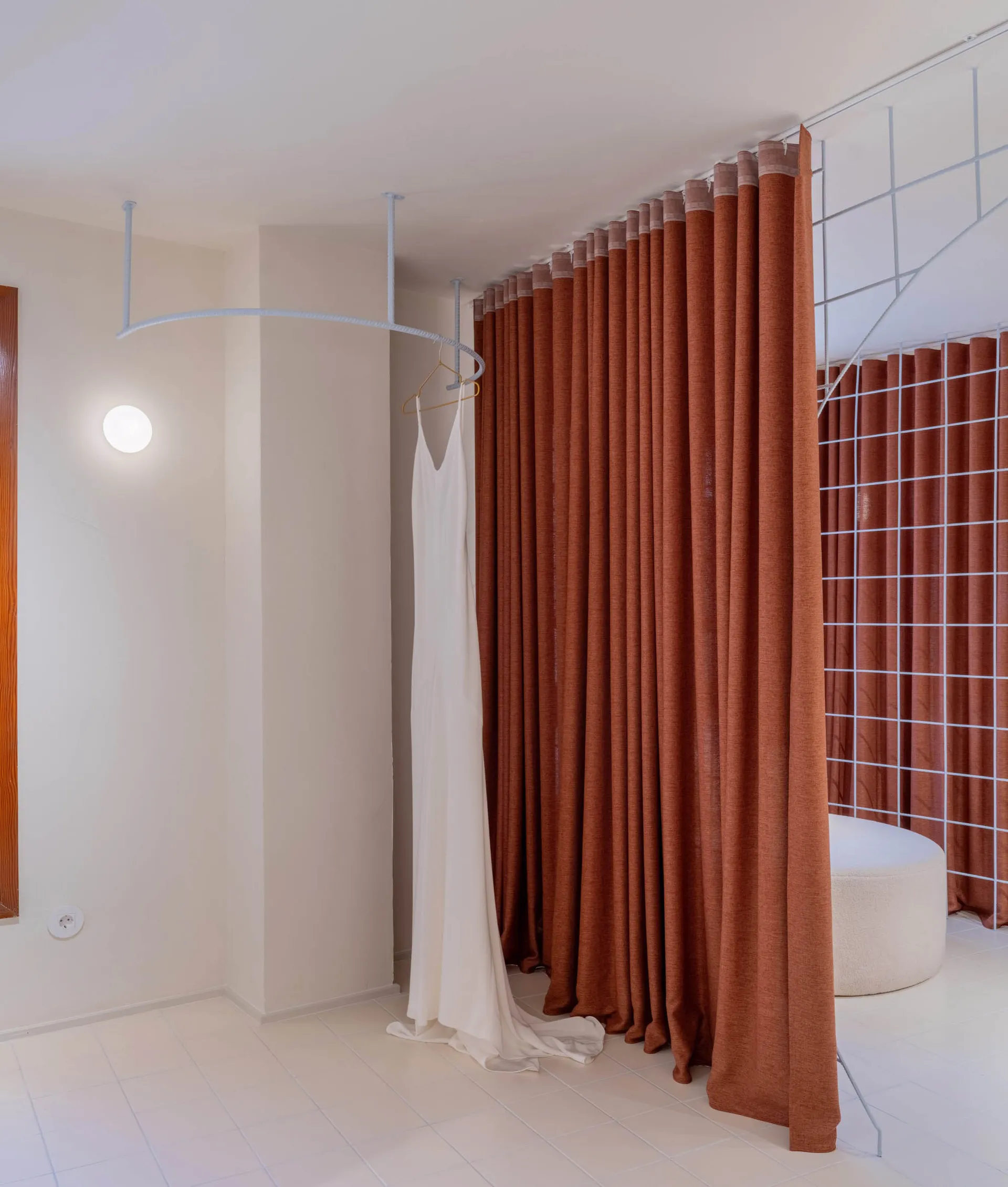 A clothing shop with a white dress hanging on a rail, surrounded by brown curtains.