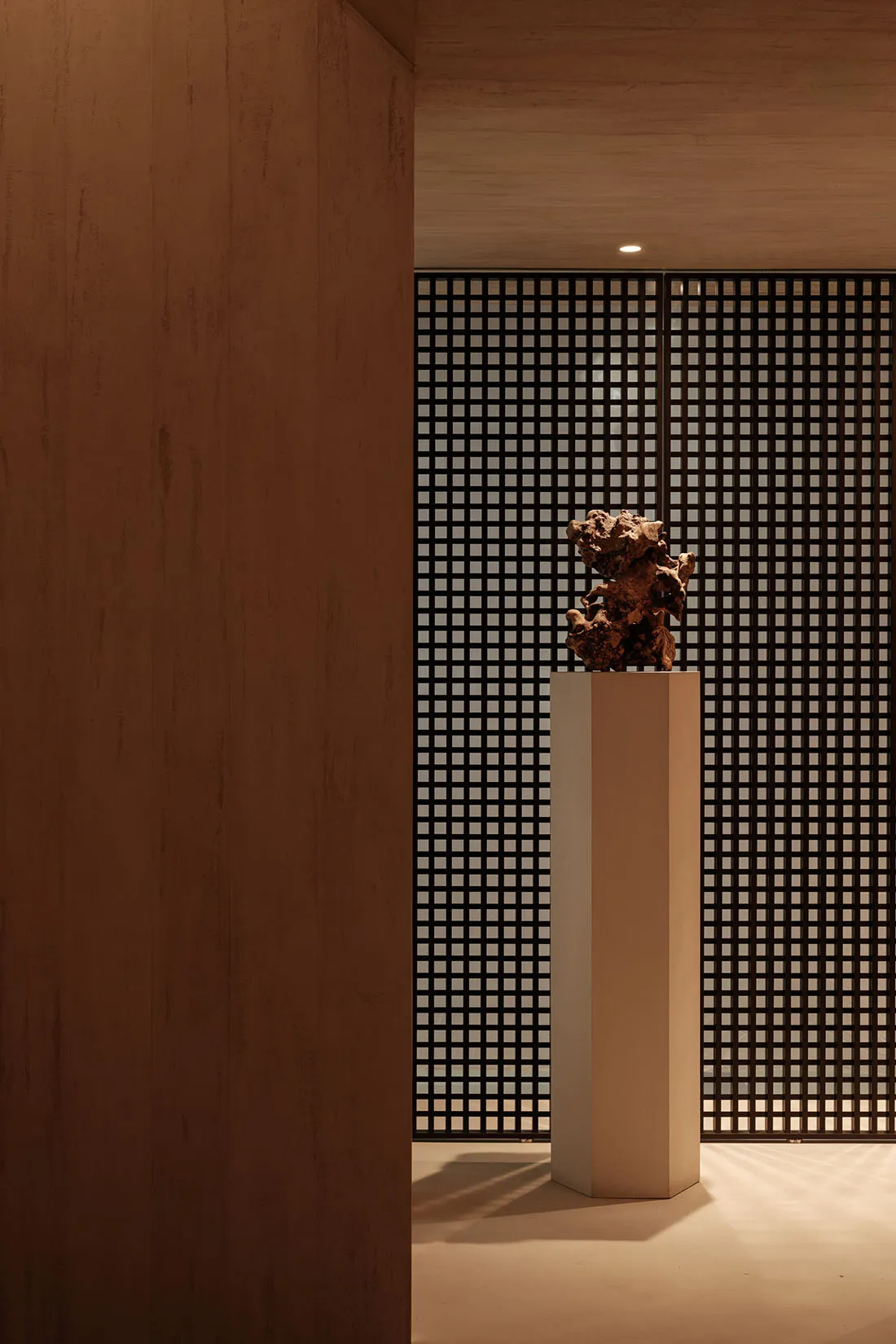 An abstract sculpture displayed on a pedestal within a modern lobby, constructed of concrete material.