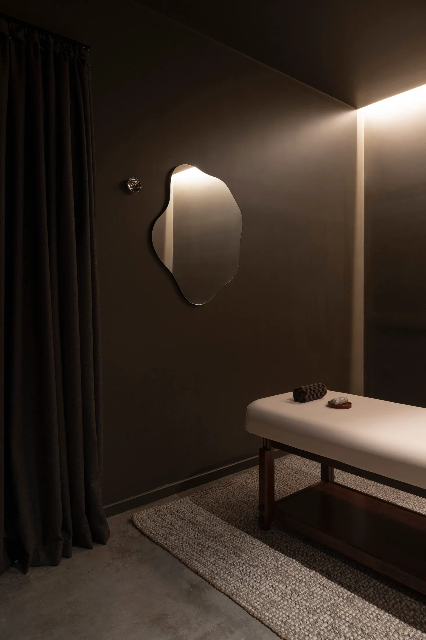 A modern spa interior with a square wall mirror, minimalist black design, and a massage bed.