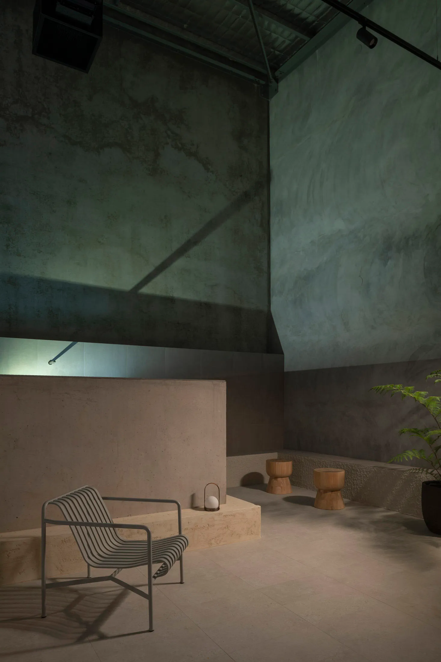 A minimalist lounge area with concrete walls and stools, featuring a striped armchair and a potted plant.