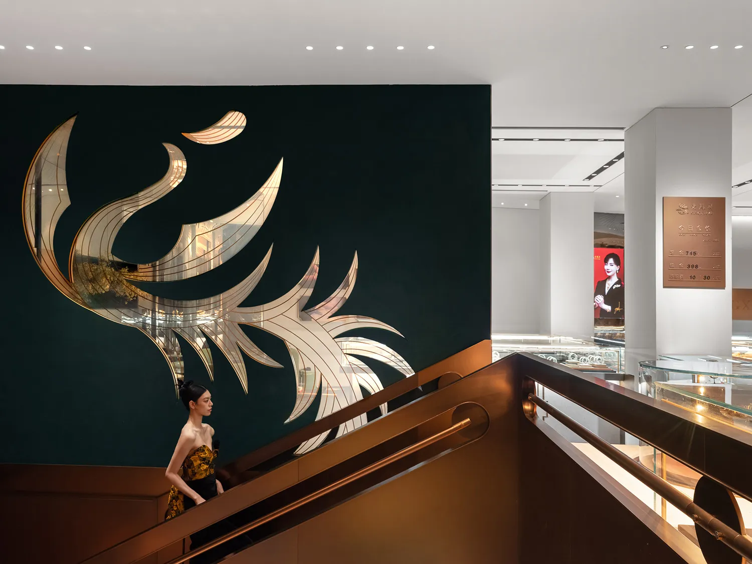 A woman in a yellow dress walking down a staircase with a metallic glazing wall and a gold-leafed phoenix artwork in a commer