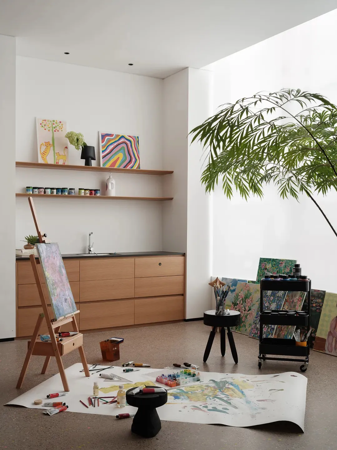 A minimalist painting studio featuring an easel, paints, and paper on the floor.