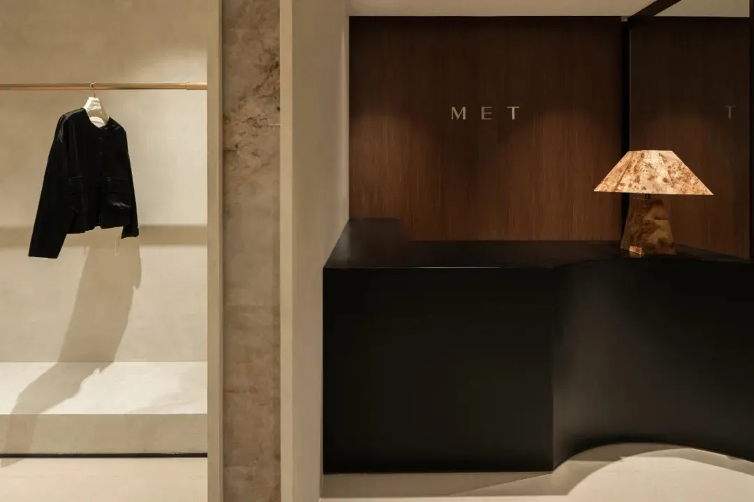 A minimalist shop interior featuring a black counter with a wood lamp, a black leather jacket hanging on a rod, and a marble