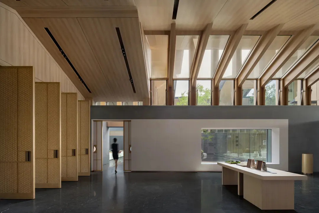A modern hotel lobby with wooden walls and ceiling, a black marble floor, and large windows.