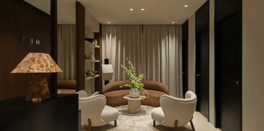 A modern neutral living room with a brown curved sofa, white armchairs, and a wooden lamp with a unique design.
