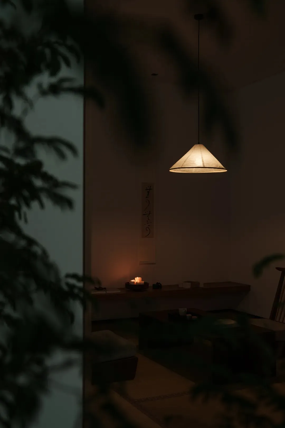 A minimalist cozy lounge area with a paper lampshade, candles, and a traditional Japanese writing scroll hanging on the wall.
