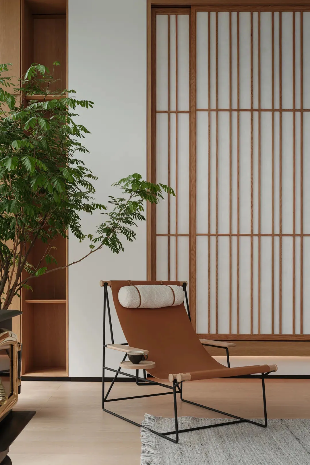 A minimalist relaxation space featuring a brown leather chair with a white cushion, a small table with a cup, and a potted pl