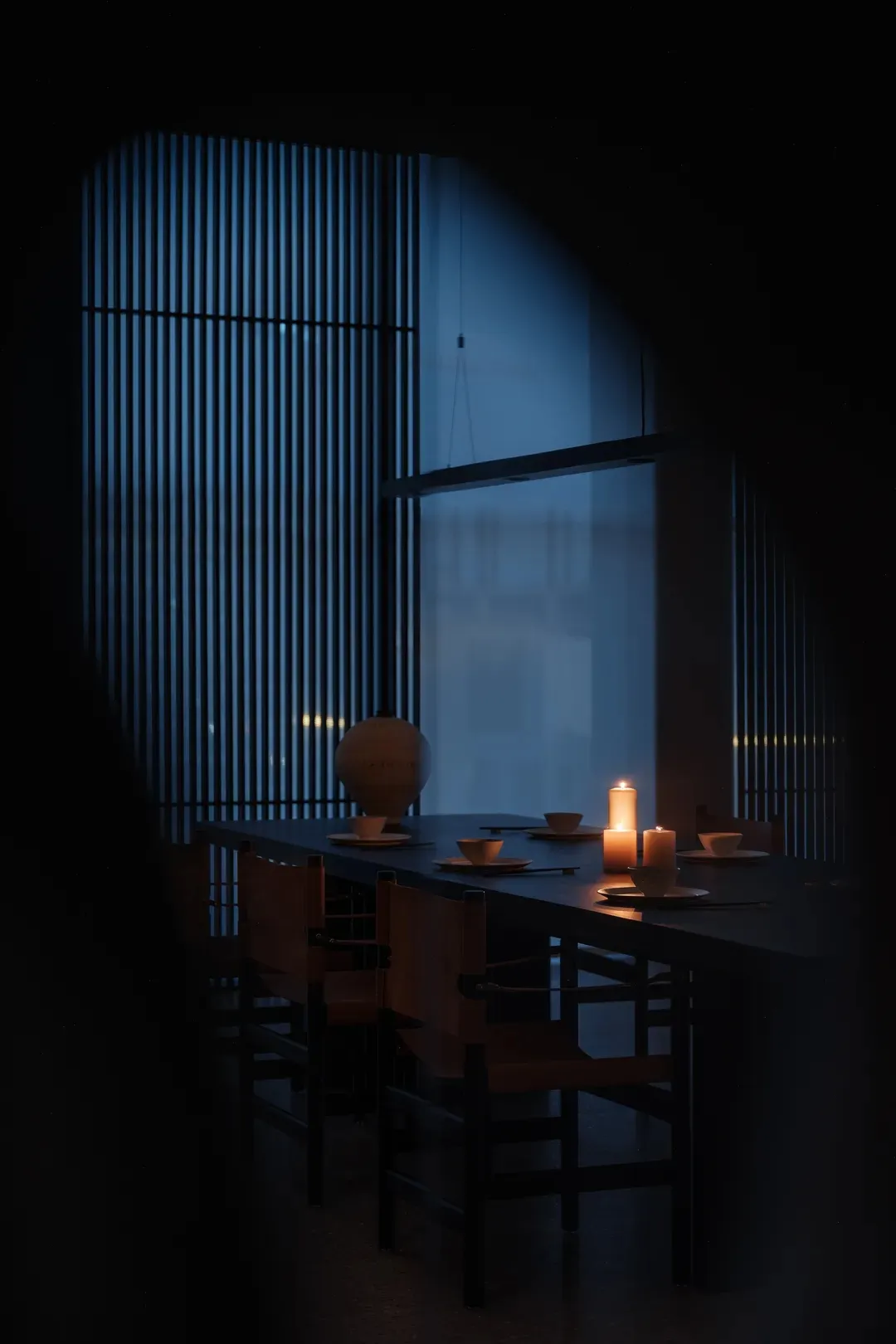 A minimalist dining room with wooden paneling and a lit candle setting the scene.
