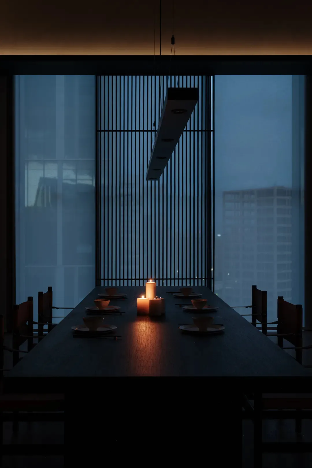 An elegant dining room with a long table set for dinner, featuring wood elements and soft candlelight.