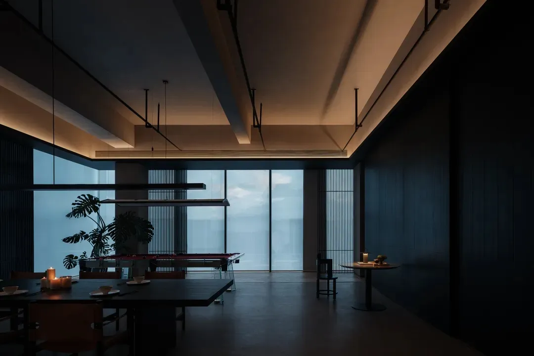 Modern industrial dining room with metal table and chairs, large floor-to-ceiling windows, and hanging lights.