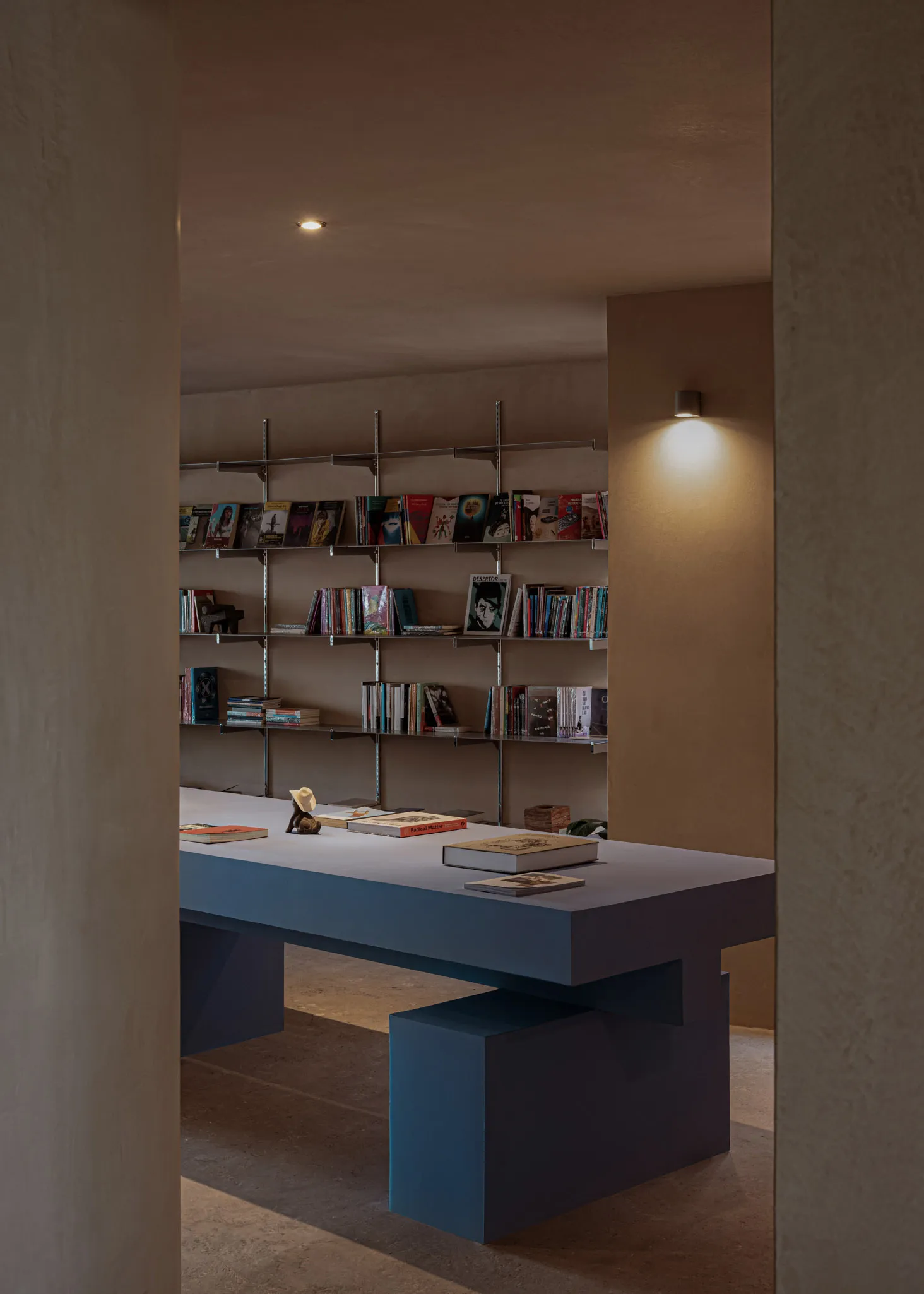 A modern bookstore with steel shelves and a concrete floor, featuring books displayed on the shelves and a desk in the foregr