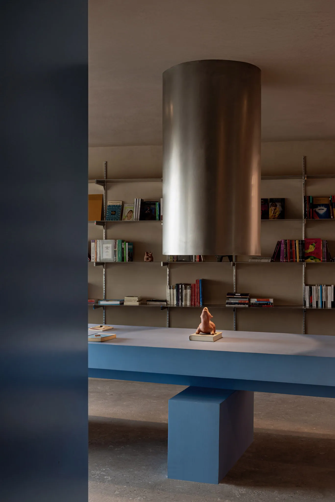 A minimalist room with a blue and metallic bookshelf, featuring a sculpture of a lion on a book.