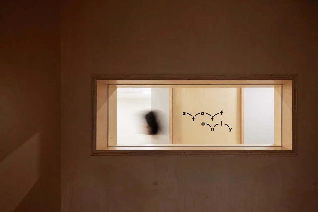 A rectangular window inset into a wooden wall, with a mural of interconnected letters inside.