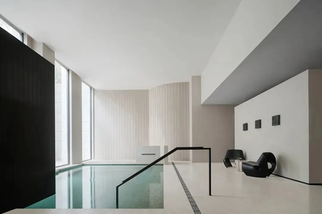 A modern indoor swimming pool with concrete flooring and minimalist design elements.
