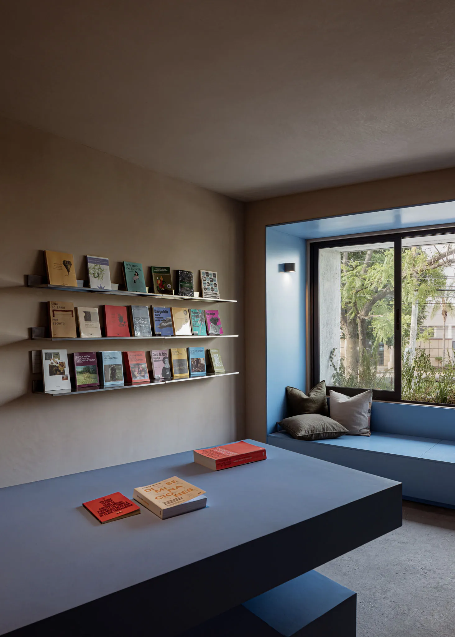 A minimalist library room with concrete walls, floating shelves, and a built-in bench seat.