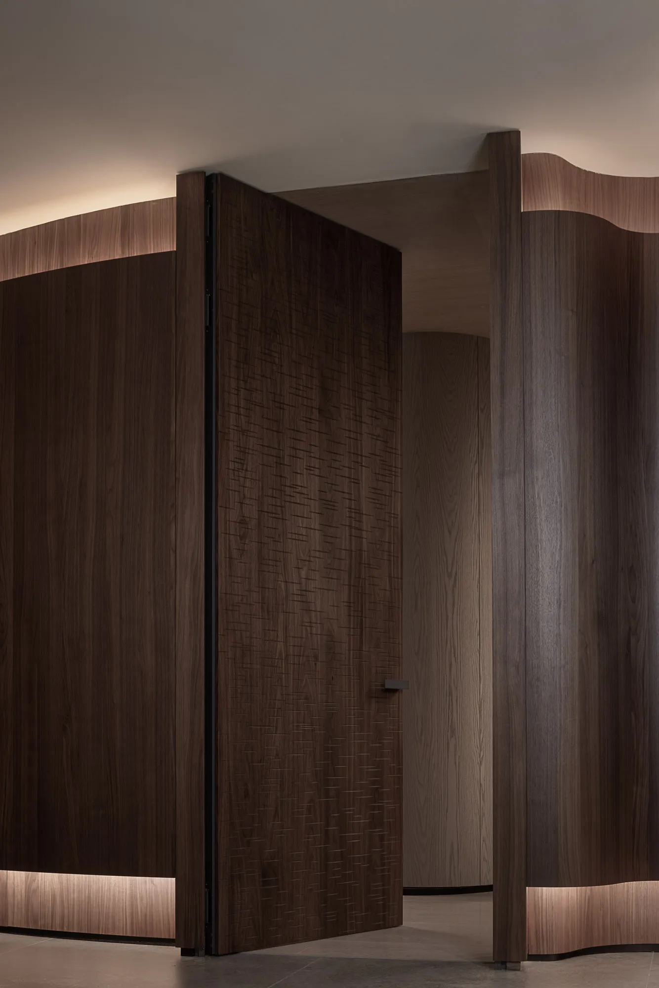A modern dark wood entrance door with a geometric pattern, illuminated by soft lighting from beneath the door frame.