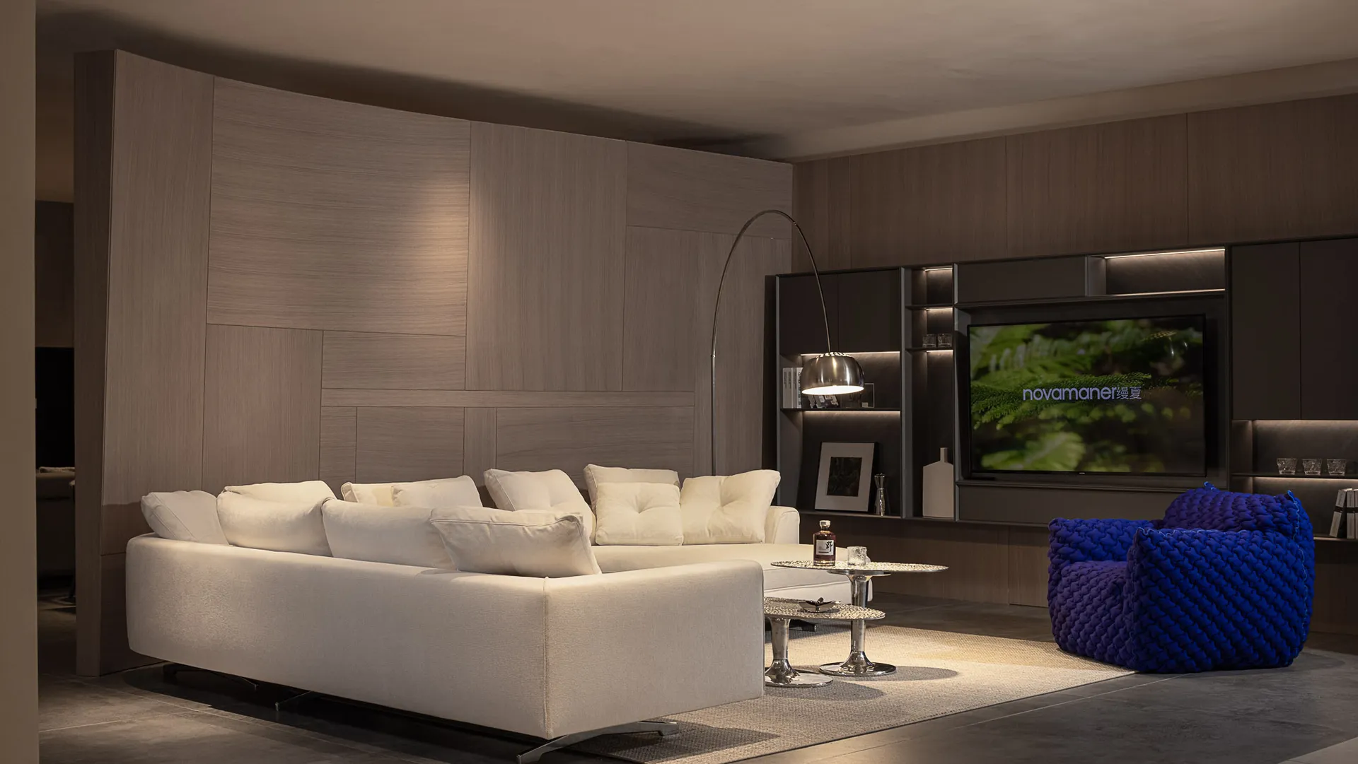 Modern living room with white fabric sofa and blue knitted chairs, wooden cabinets, and a flat-screen TV.