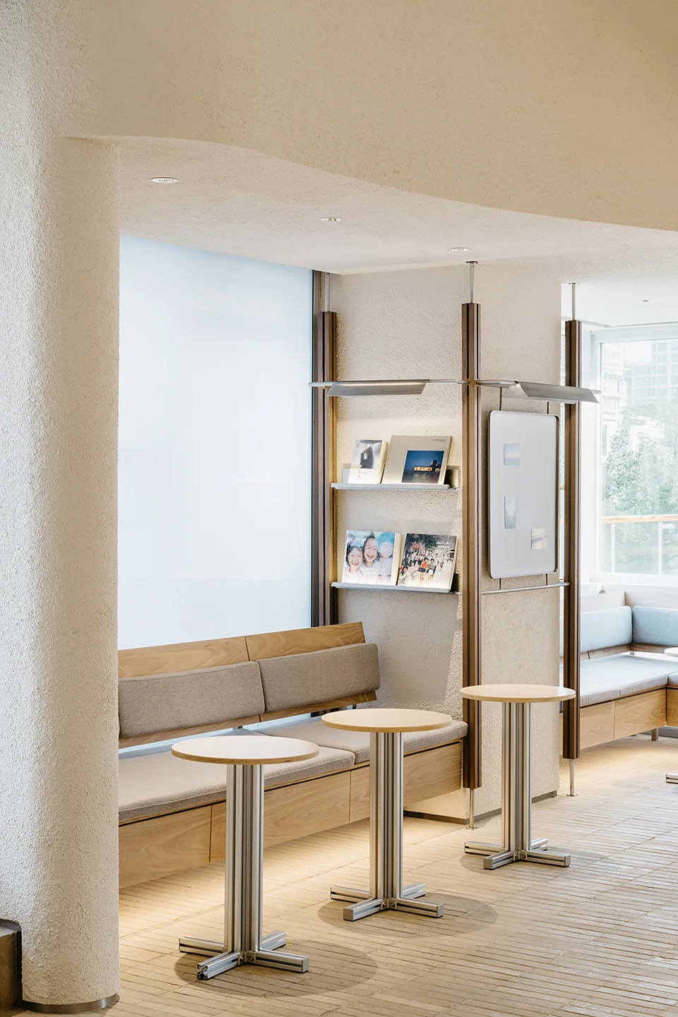A modern reception area with wooden tables, a wooden bench, and metal shelving.