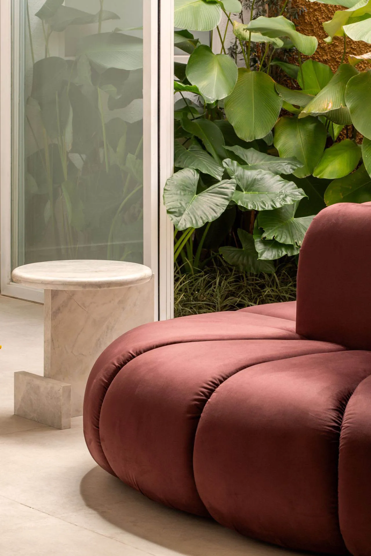 Modern living room with a fabric sofa surrounded by green plants.