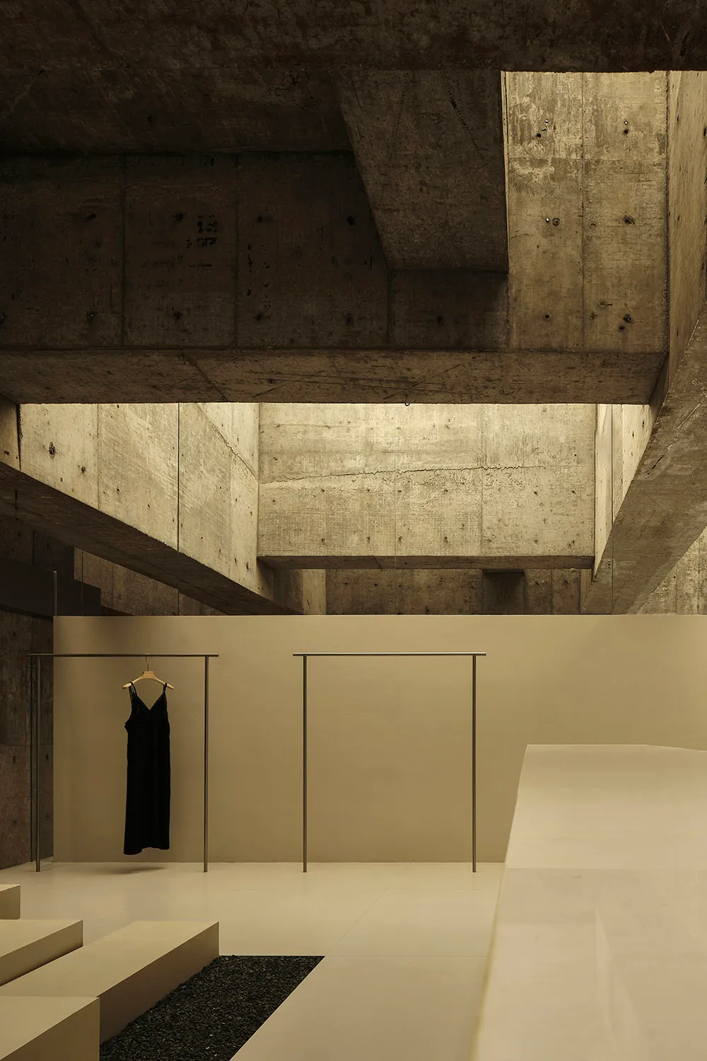 A minimalist clothing shop featuring black dresses hanging on racks with concrete walls and metal elements.