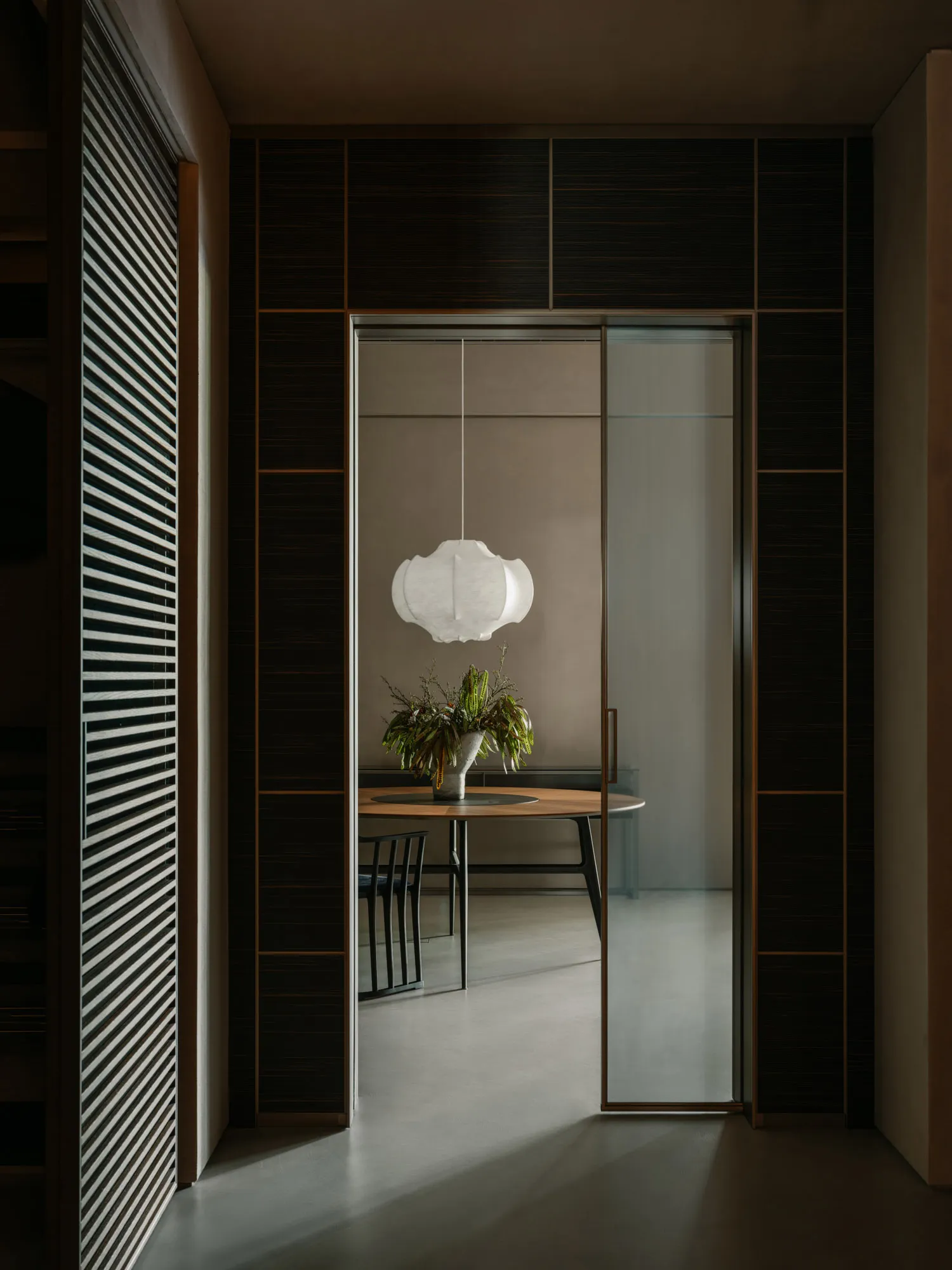 Modern minimalist dining room with a wooden table, a hanging pendant lamp, and a houseplant.