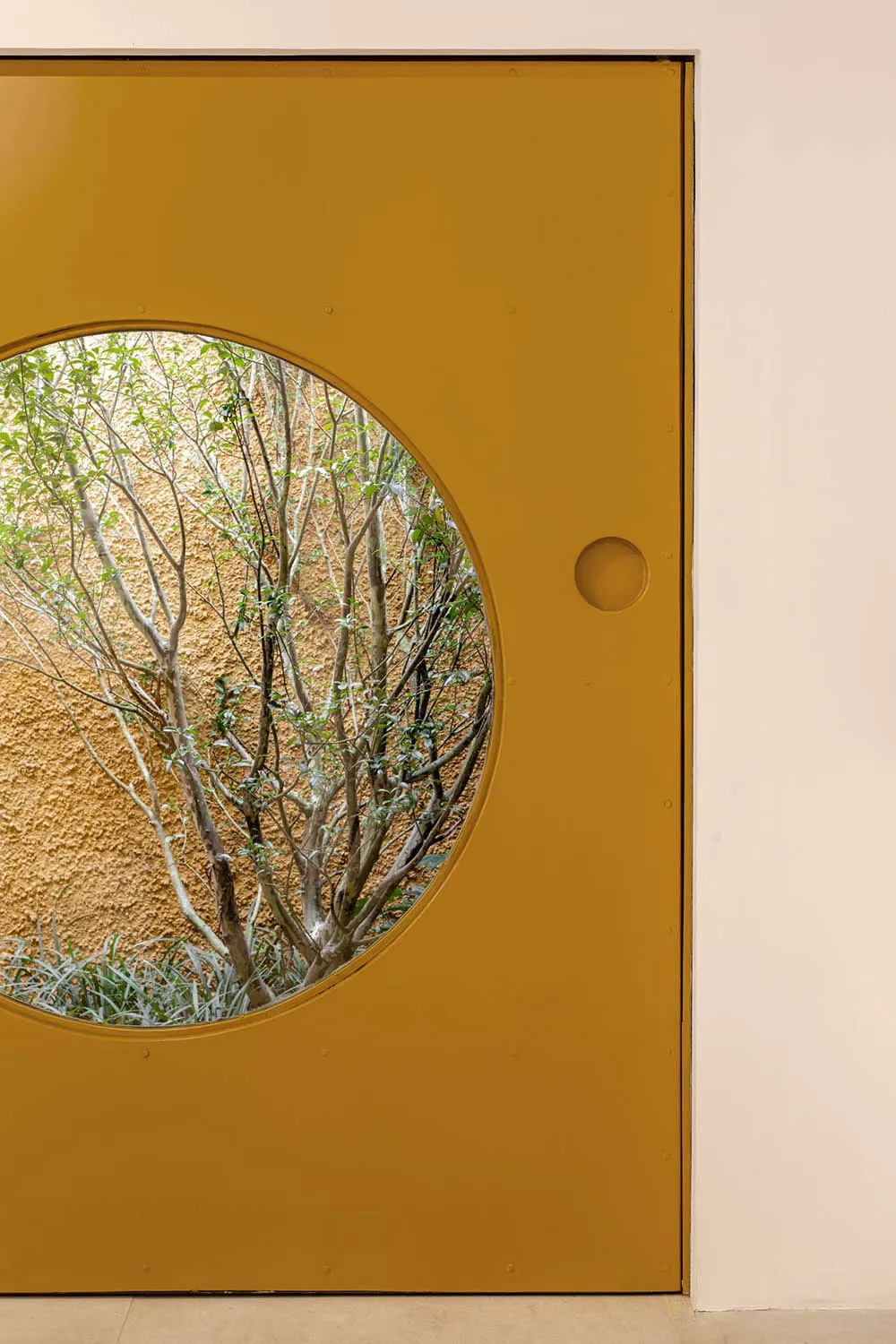 A modern interior design featuring a striking yellow door with a circular window, framed by a white wall.