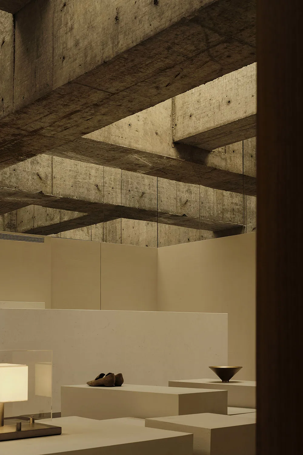 A minimalist interior space featuring concrete walls and ceiling beams, with simple furniture and decorative objects.