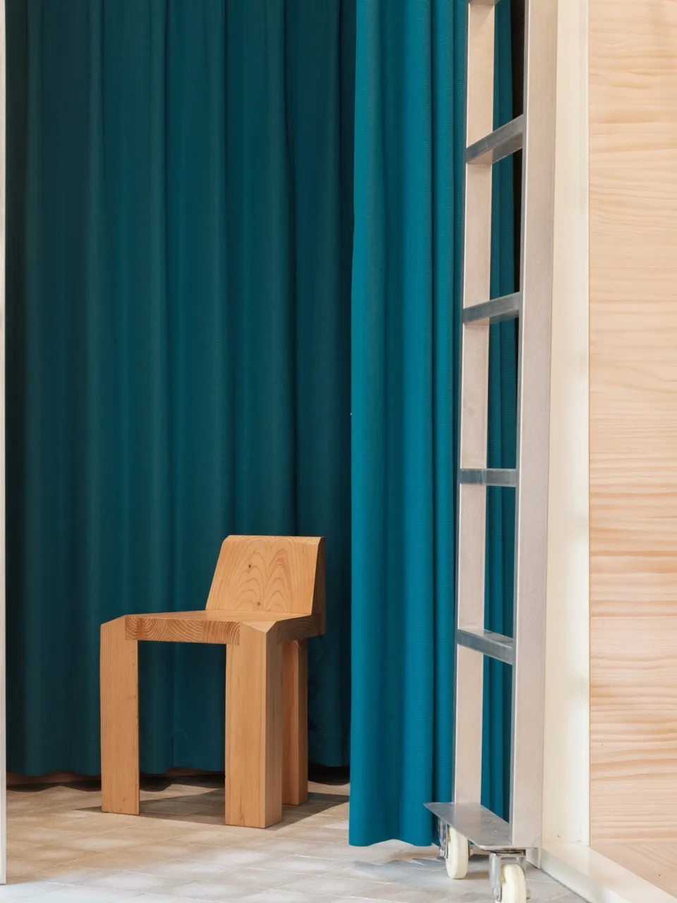 A minimalist wooden chair in front of a blue curtain.
